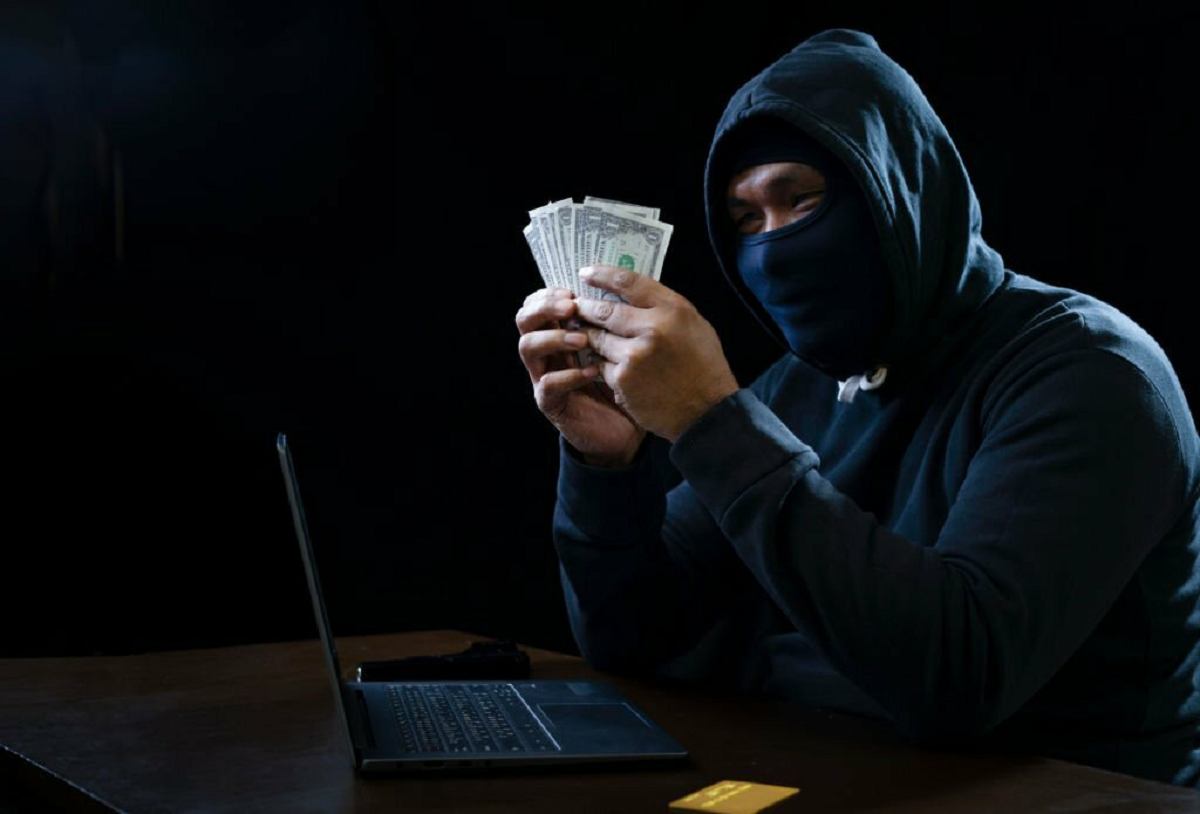 Photo of a hacker in hoodie using laptop.